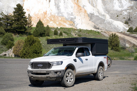 White Ford Ranger pickup with black overland camper, parked by nature's travertine terraces. An ideal RV rental for adventure.