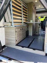 Explore this rv rental's adaptable interior: a stowed bed, pop-up table with mugs, and light wood cabinetry for smart storage.