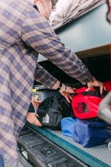 Hands load North Face duffel bags into an RV rental's clever storage, ideal for adventure travel gear.