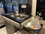 This RV rental kitchenette features dark counters, brushed cabinets, a sink, stovetop with kettle, and a coffee/tea station.