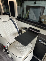 Enjoy luxury travel in this RV rental with a comfortable white leather seat, fold-out table, and integrated entertainment system.
