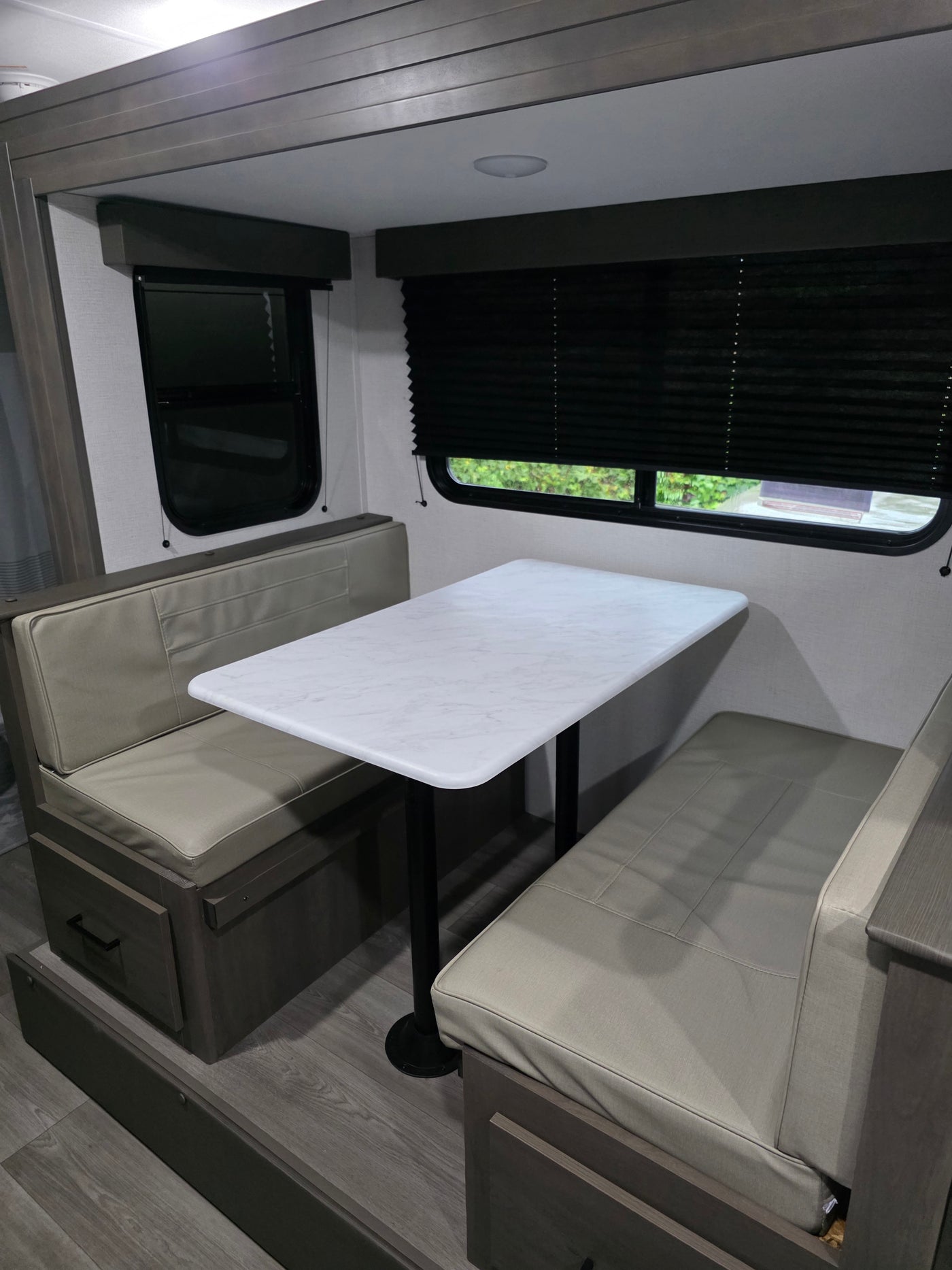 This RV rental dinette features cozy, light-colored cushioned benches, a white marble-patterned table, and dark wood accents. — photo 6