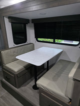 This RV rental dinette features cozy, light-colored cushioned benches, a white marble-patterned table, and dark wood accents.