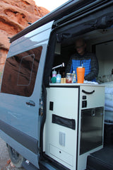 Man inside a grey **rv rental** van with an open side door, showcasing the built-in kitchen and countertop.