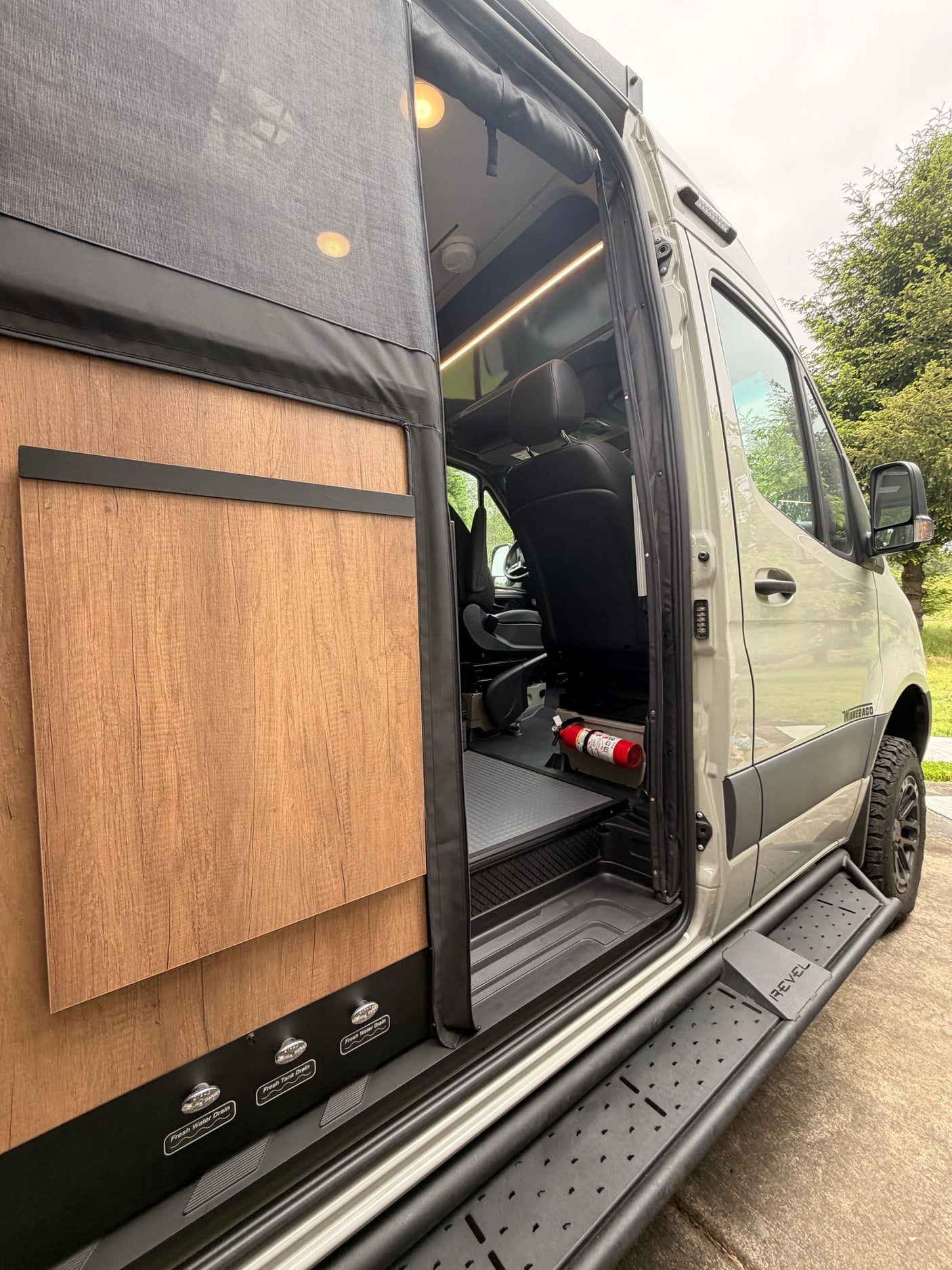 Winnebago Revel RV rental with an open side door, showcasing its modern interior, steps, and utility controls for a camper van.