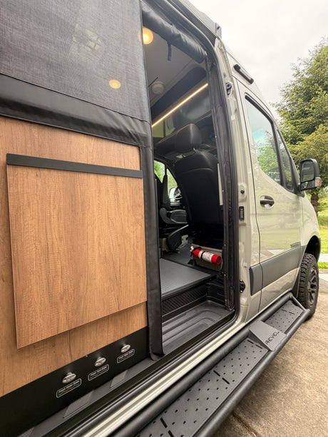 Winnebago Revel RV rental with an open side door, showcasing its modern interior, steps, and utility controls for a camper van.