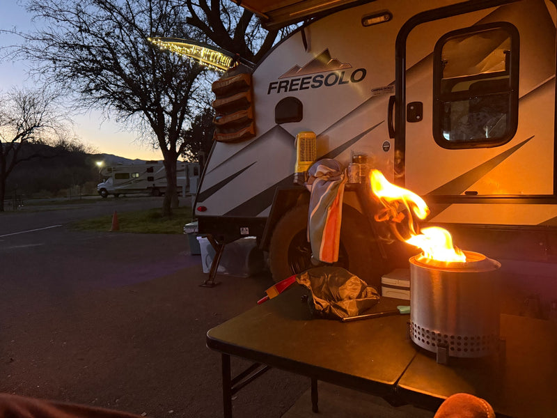 Our RV rental Freesolo trailer at dusk, with a tabletop fire pit casting warm light on the scene and string lights on the awning. — photo 4