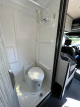 Inside an rv rental: a pristine, compact white wet bath featuring a toilet, shower, and floor drain.