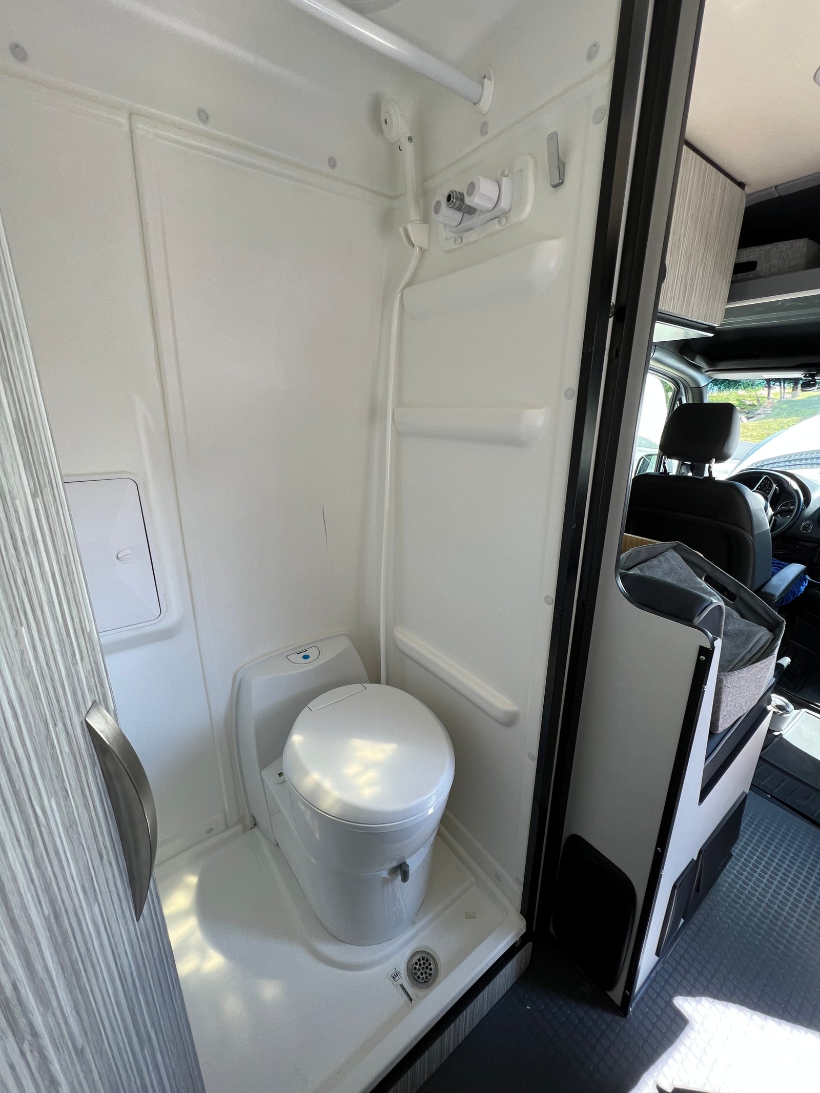 Inside an rv rental: a pristine, compact white wet bath featuring a toilet, shower, and floor drain.