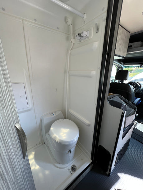 Inside an rv rental: a pristine, compact white wet bath featuring a toilet, shower, and floor drain.