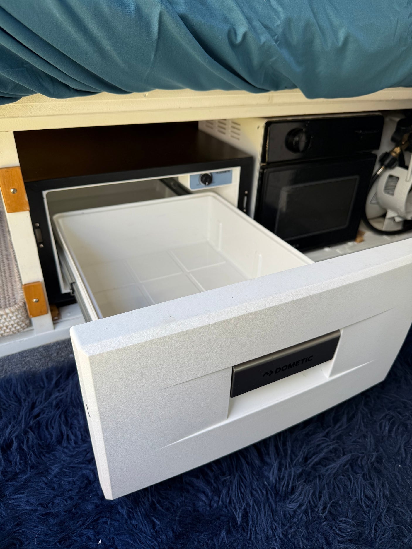 Open Dometic drawer fridge in a compact rv rental camper van kitchen setup, with a dark blue shag rug floor. Ready for adventures!