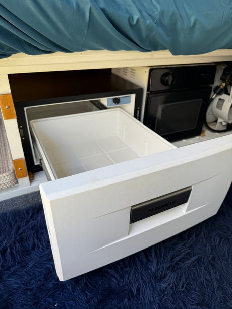 Open Dometic drawer fridge in a compact rv rental camper van kitchen setup, with a dark blue shag rug floor. Ready for adventures!