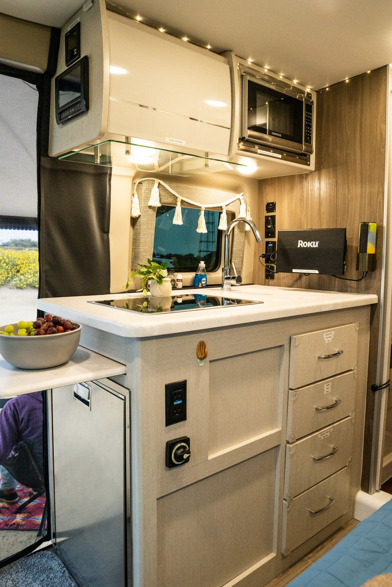 Inside an rv rental, showing a modern kitchen setup with sink, microwave, drawers, and pull-out counter with fruit. — photo 16