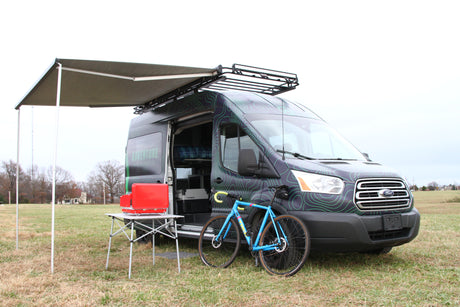 Adventure rv rental van, with graphic design, awning, bike, & camp setup in a field. Perfect for outdoor travel.