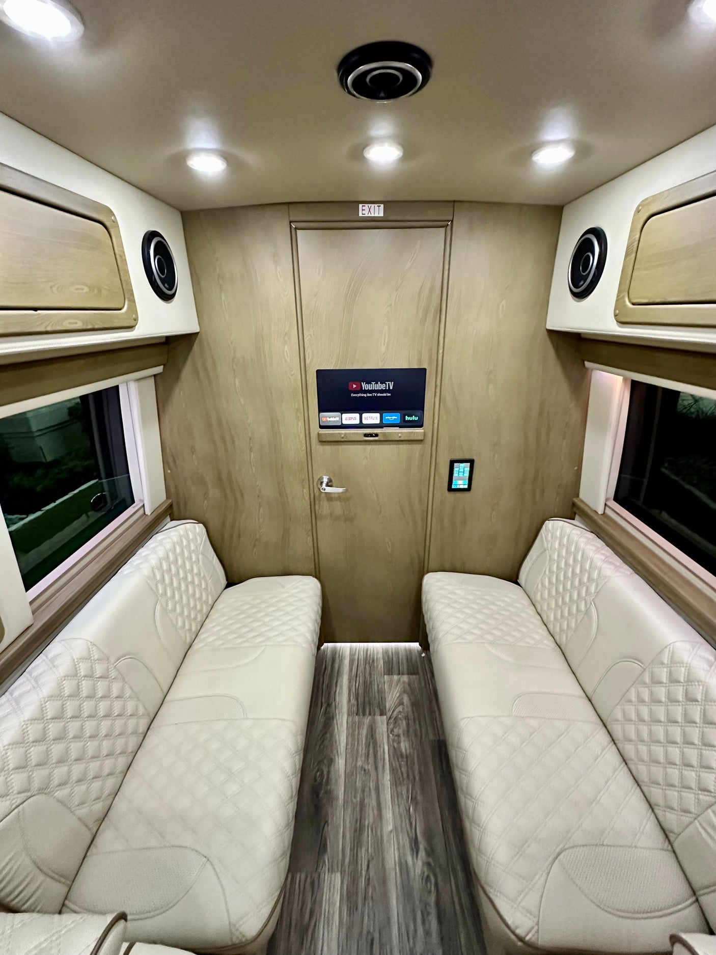 Luxury RV rental interior with plush, diamond-stitched seating, smart TV, and elegant wood-paneled walls.