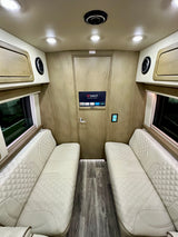 Luxury RV rental interior with plush, diamond-stitched seating, smart TV, and elegant wood-paneled walls.