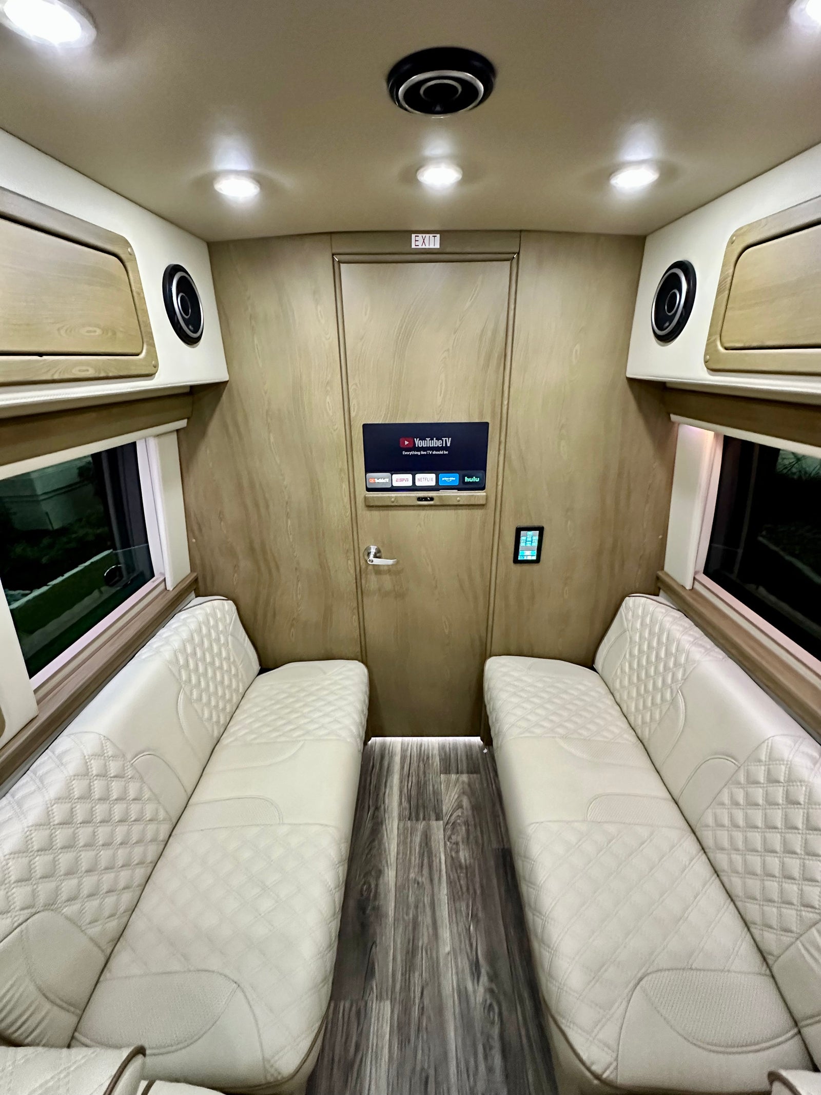 Luxury RV rental interior with plush, diamond-stitched seating, smart TV, and elegant wood-paneled walls.