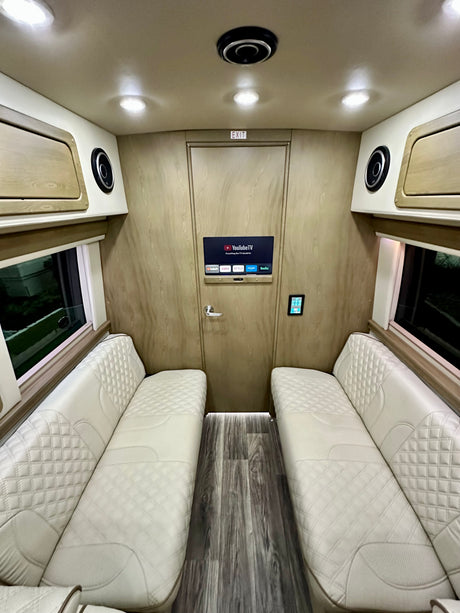 Luxury RV rental interior with plush, diamond-stitched seating, smart TV, and elegant wood-paneled walls.