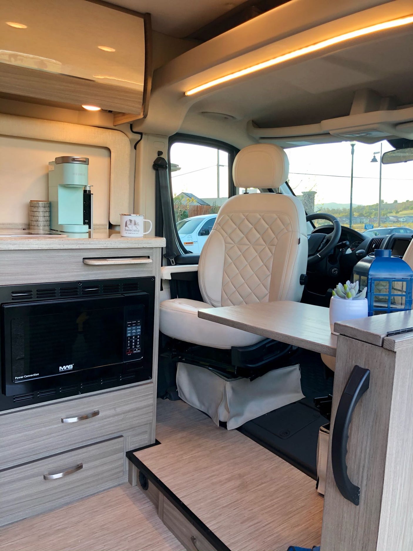 This modern RV rental features a compact kitchenette with microwave, Keurig, and a swiveling passenger seat for comfortable living.