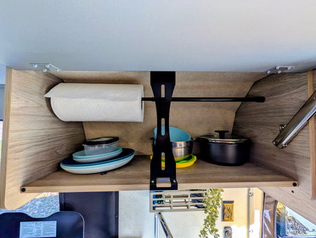 Organized RV rental kitchen cabinet with paper towels, stacked plates, bowls, and cooking pots for efficient travel.