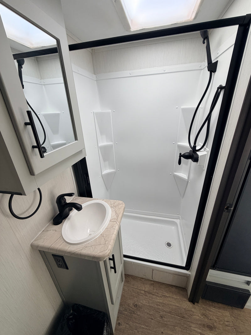 Bright, modern RV rental bathroom. Features a white shower with black-framed door, skylight, sink vanity, & wood-look floor. — photo 10