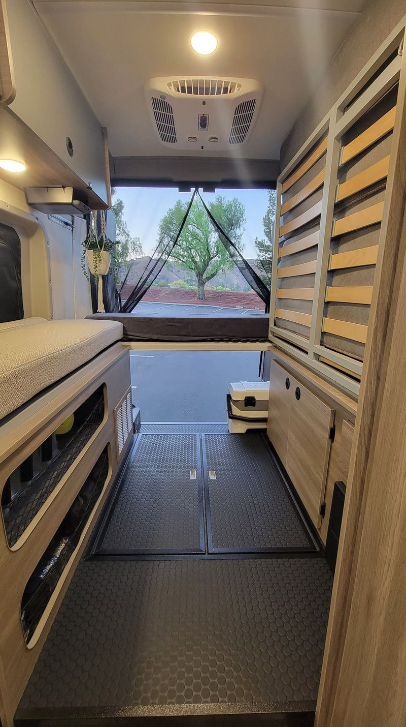 Inside an RV rental: Rear view showing bed, storage, and open doors with bug screen to nature. AC unit on ceiling. — photo 4