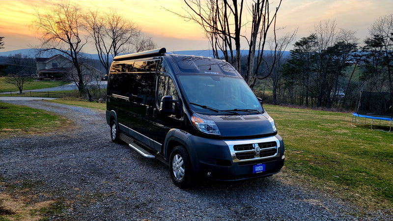 Black Sunlight camper van (RV rental) parked on a gravel driveway at sunset, with a house and mountains in the scenic background. — photo 3