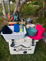 This RV rental kitchen setup includes dishware, utensils, and cleaning supplies on a portable cooler, perfect for camping.