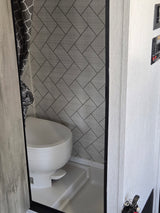 RV rental's compact wet bath features a toilet, shower, and modern grey patterned walls with a stylish curtain.