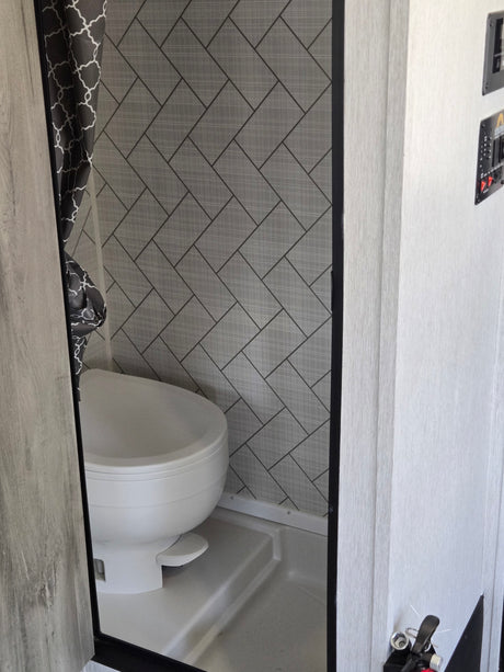 RV rental's compact wet bath features a toilet, shower, and modern grey patterned walls with a stylish curtain.