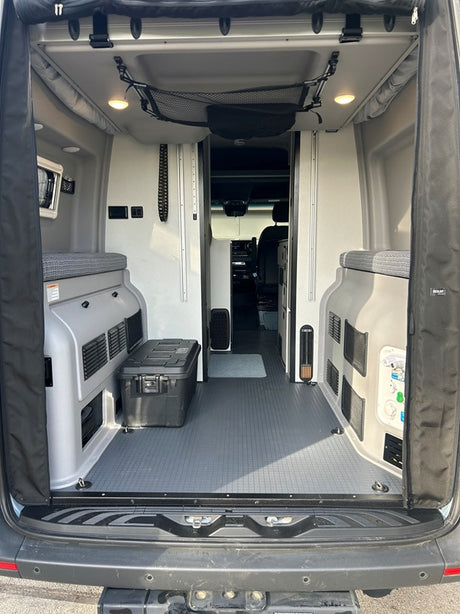 View from the open rear doors of an RV rental, revealing the versatile camper van interior with seating, storage, and utility connections.