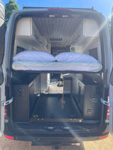 Inside a modern rv rental camper van, featuring an elevated bed, pull-out cargo tray, custom cabinets, and essential controls.