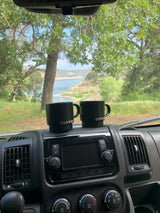 Perfect RV rental morning with two 'COFFEE' mugs & scenic lake view through windshield.