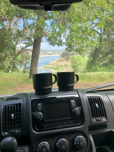 Perfect RV rental morning with two 'COFFEE' mugs & scenic lake view through windshield.