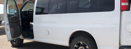 White van RV rental, side view, door open. Features off-road tires, hinting at adventure readiness.