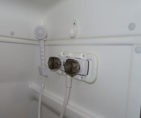 RV rental shower interior: white, compact, featuring a handheld sprayer and dual faucet controls.
