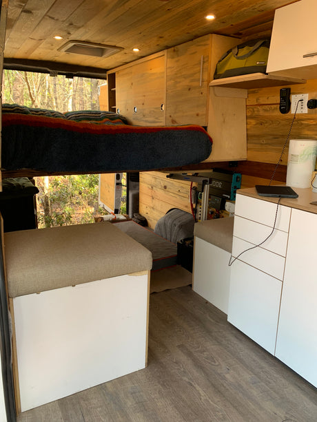 Inside a well-appointed rv rental camper van, featuring a raised bed, wood-paneled walls/ceiling, and a compact living space.