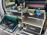 Compact RV rental kitchen setup with propane stove, sink, and cooking essentials. Perfect for camping meals.