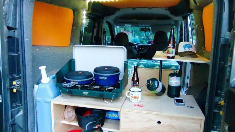  and a wooden table.|Inside an RV rental: a van's cozy bed with red quilt — photo 3