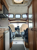 Cozy rv rental interior, showing a compact kitchen with a microwave and refrigerator, and the driver's area beyond.