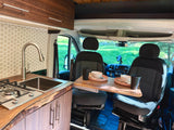 RV rental: A cozy camper van kitchen with live-edge counter, sink, stove, and dining table set with swivel front seats.