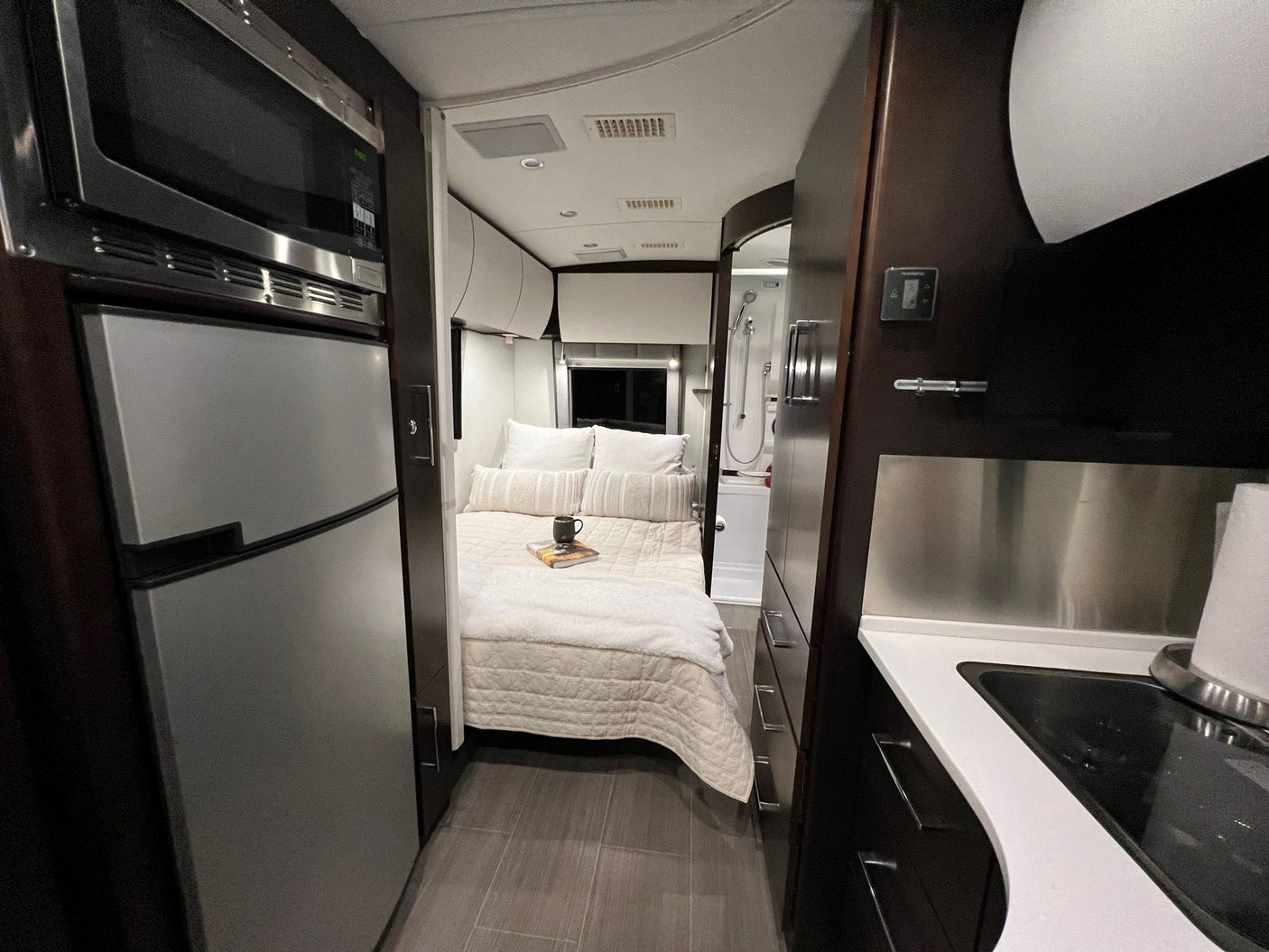Cozy, modern RV rental interior features a compact kitchen with a sink, central bedroom, and rear bathroom with a shower.