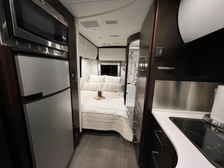 Cozy, modern RV rental interior features a compact kitchen with a sink, central bedroom, and rear bathroom with a shower.