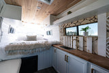 Inside a modern RV rental: comfy bed, compact kitchen with wood counters, and stylish wood wall accents.