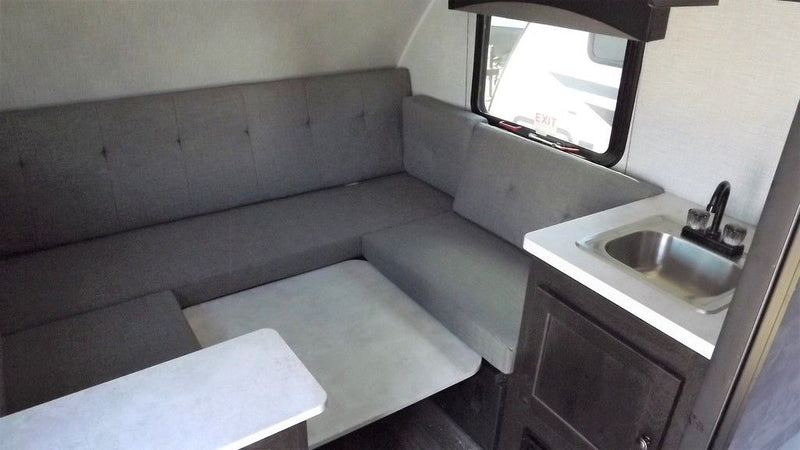  neatly lined up on a sunny gravel lot.|This RV rental interior showcases an L-shaped grey dinette — photo 2