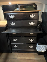 Black upcycled dresser with ornate handles and a pull-out desk, integrated into an RV rental for compact storage.