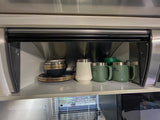 Neatly organized RV rental kitchen cupboard with stacked black/gold plates, a blue bowl, white mug, and green Stanley mugs.