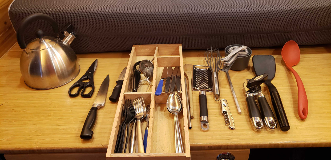 RV rental kitchen essentials: kettle, knives, cooking utensils, measuring cups, and tools arranged on a counter.