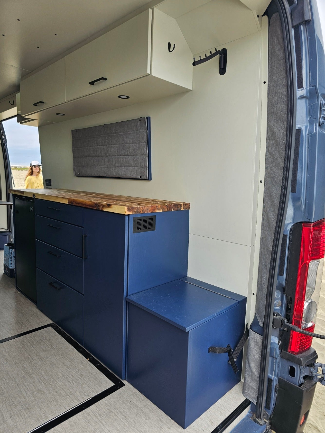 Inside this custom RV rental, a compact kitchen with navy cabinets, wood counters, and storage awaits adventurers.
