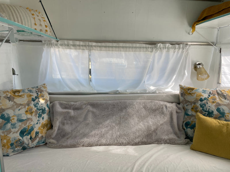 Comfortable RV rental sleeping nook featuring bright floral pillows, soft gray throw, and sheer white curtains. — photo 9